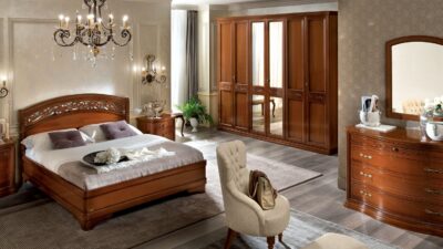 Walnut Torriani bedroom suite with carved headboard, nightstands and a mirrored wardrobe in a styled room.